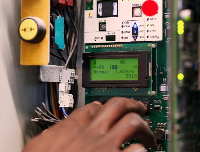 Placa de control de ascensor con pantalla LCD y una mano configurando parámetros